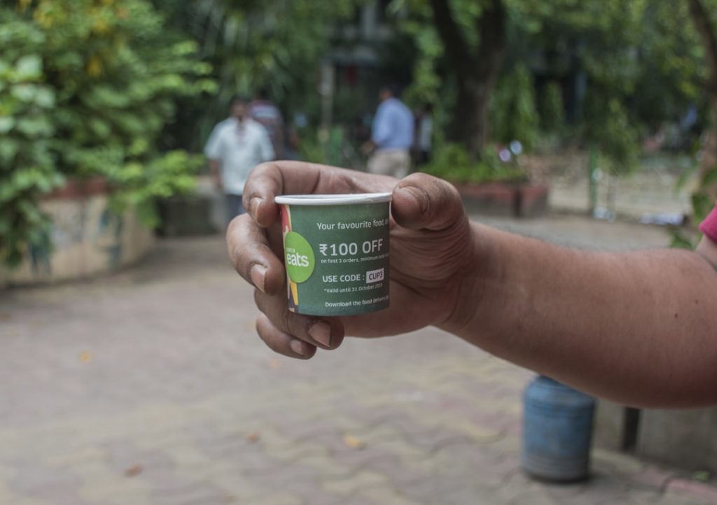 A man holiding a branded paper cup in his hands that is displaying a coupon code offer by UberEats