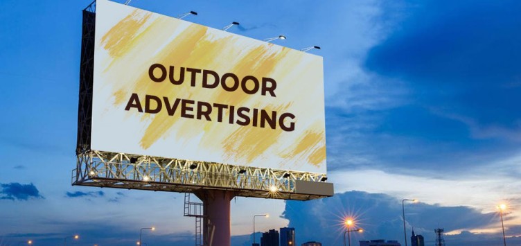 This image shows a hoarding with outdoor advertising written on it with black on a yellow sprayed background