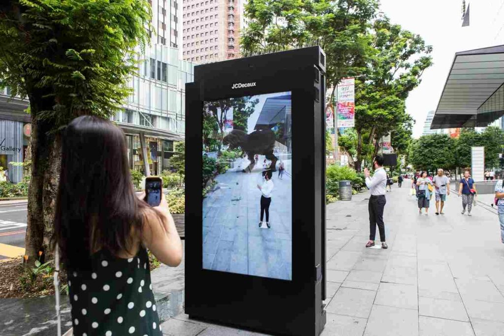 This image shows a woman with a phone capturing a man through a screen with a Dinosaur reflection