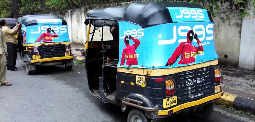Auto Rickshaw Transit Advertising Auto rickshaws parked on a city street with rear-panel advertisement wraps displaying a fashion campaign in bright blue and red colors.