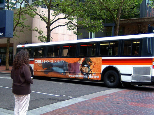 Kaiser Permanente Bus Wrap Advertisement City bus wrapped with a Kaiser Permanente health campaign advertisement reading “Chill Frequently,” parked at an urban intersection.