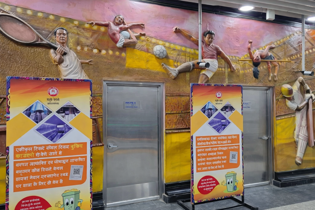 Sports-themed wall mural with athletes in action and two freestanding information boards inside a metro station