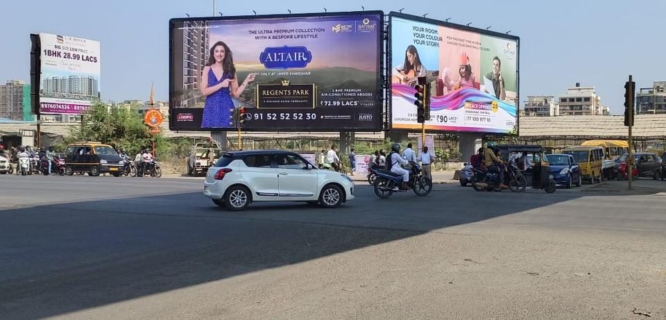 Large dual-sided billboards at a busy urban intersection featuring real estate and lifestyle advertisements, with cars, auto-rickshaws, and motorbikes navigating the junction.