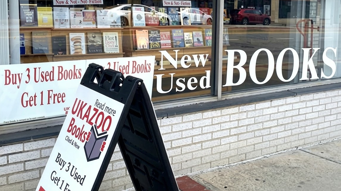 Bookstore Retail Signage and Sidewalk Promotion Bookstore window displaying “New Used Books” signage with a sidewalk stand promoting buy three get one free offer.