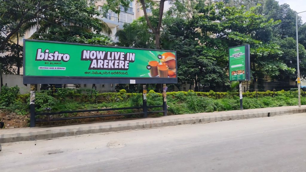 Bistro by Blinkit Outdoor Billboard Campaign Green roadside billboard promoting Bistro by Blinkit announcing “Now Live in Arekere” along a tree-lined urban street.