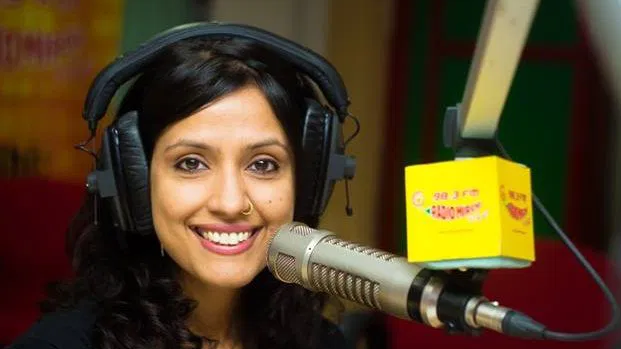 Radio Jockey Hosting a Live Radio Show in Studio Female radio host wearing headphones speaking into a studio microphone during a live broadcast at a radio station.