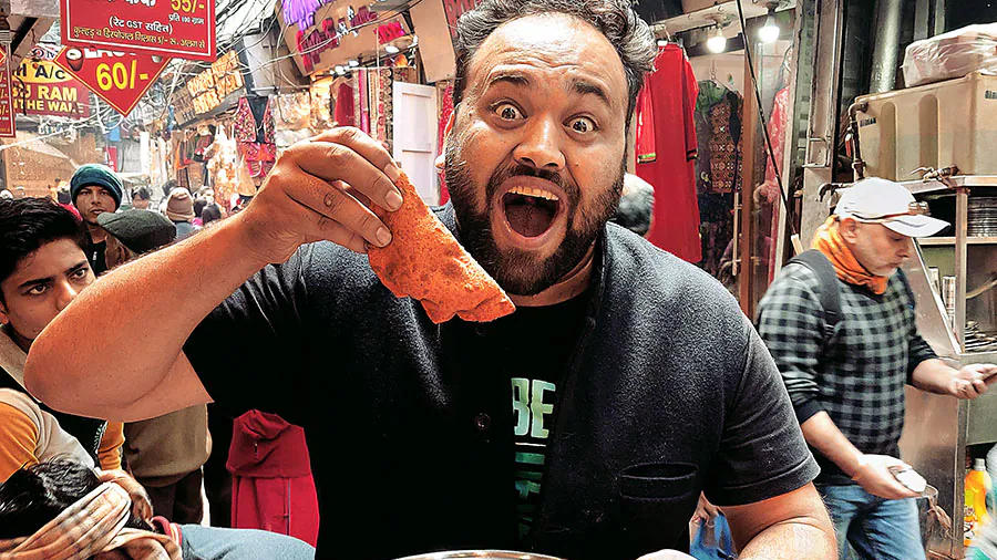 Indian Street Food Experience at Busy Local Market Man excitedly holding a dosa and thali plate while eating at a busy Indian street food market surrounded by vendors and shoppers.