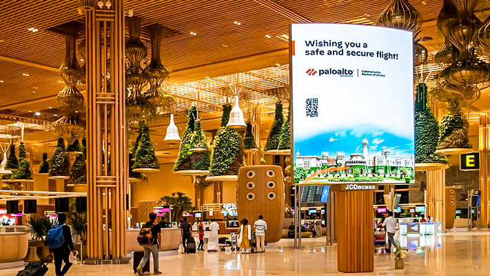 Palo Alto Networks Airport Digital Advertising Display Large vertical digital advertising screen inside an airport terminal displaying a Palo Alto Networks message wishing travelers a safe flight.