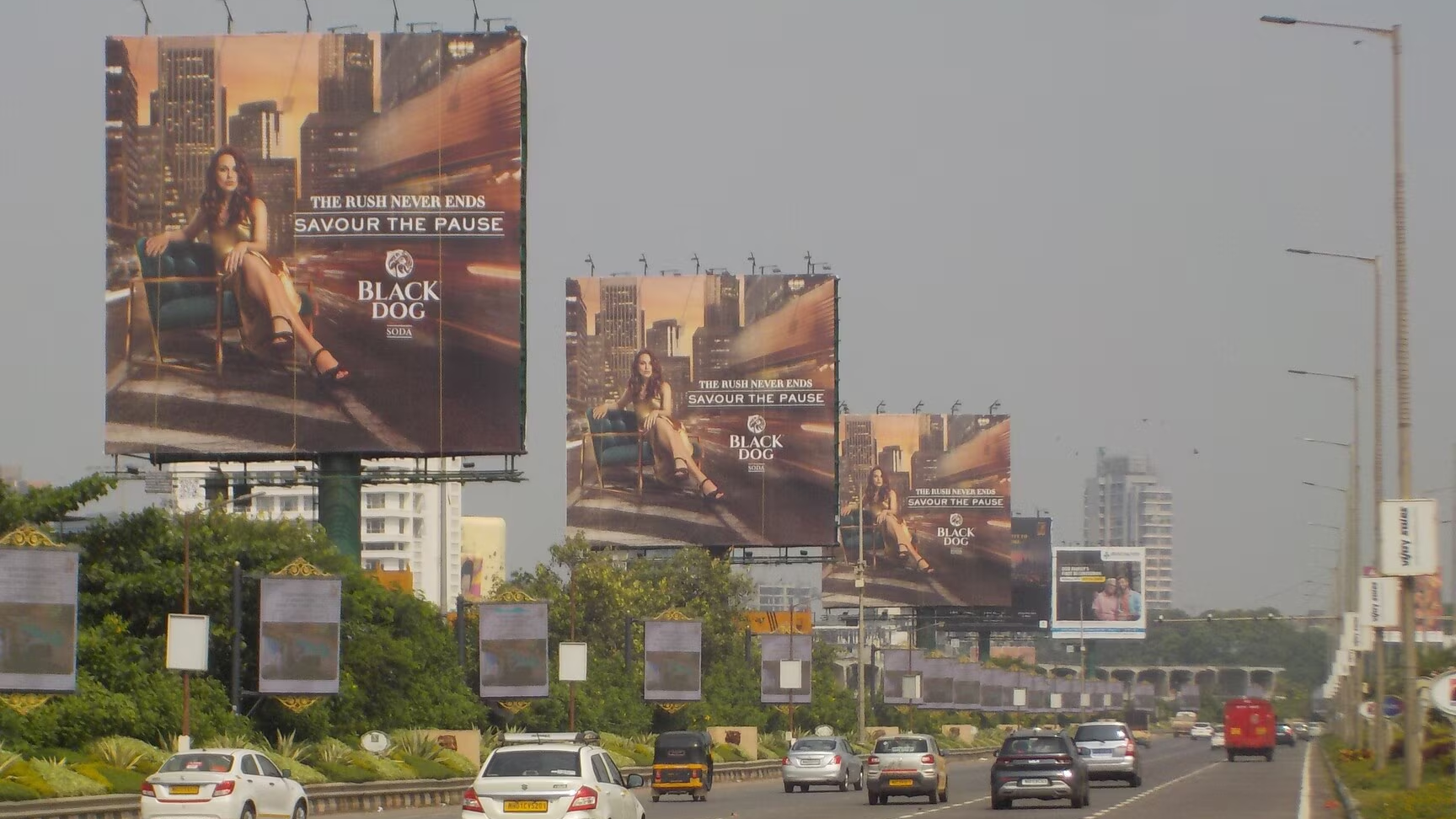 Black Dog Large-Format Highway Billboard Campaign Multiple large-format Black Dog whisky billboards displayed along a busy urban highway with moving traffic and city buildings in the background.